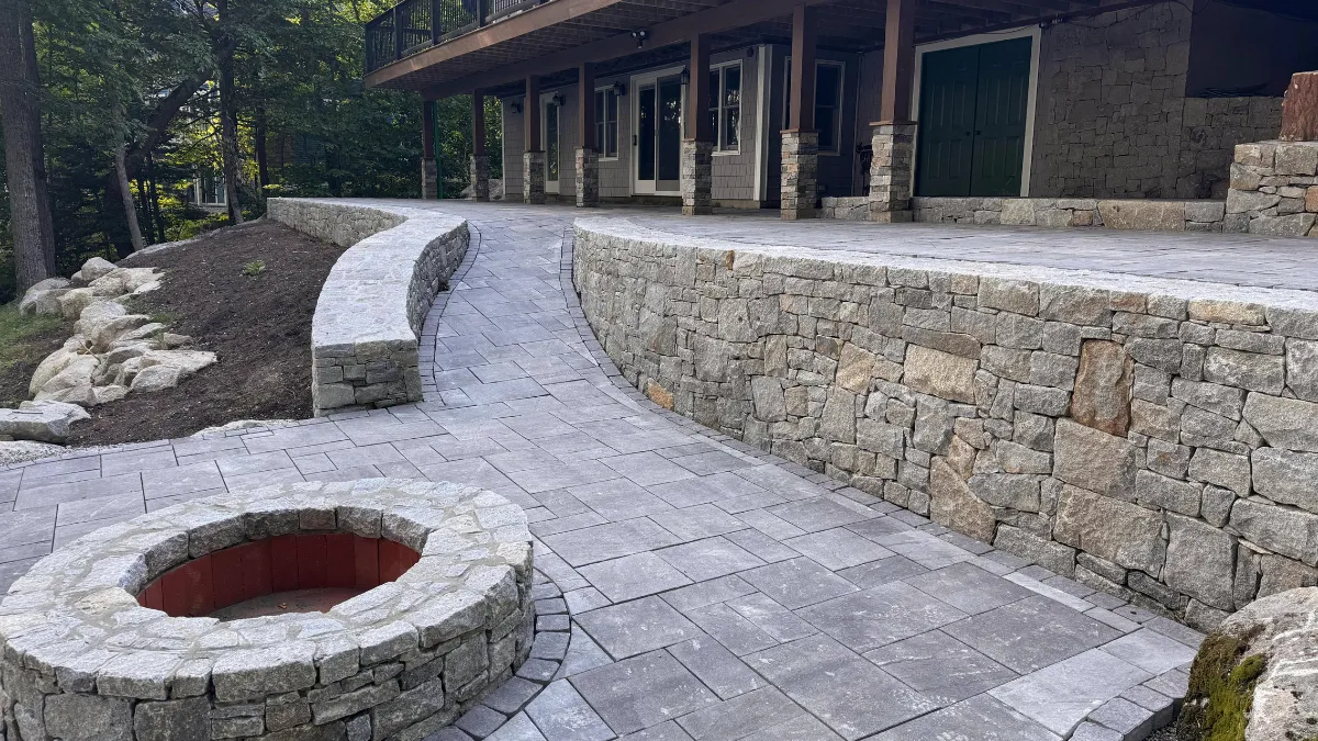 Curved stone walkway leading to a raised patio area, featuring a fire pit and surrounded by natural landscaping, illustrating thoughtful outdoor design by Maine Outdoor Spaces.